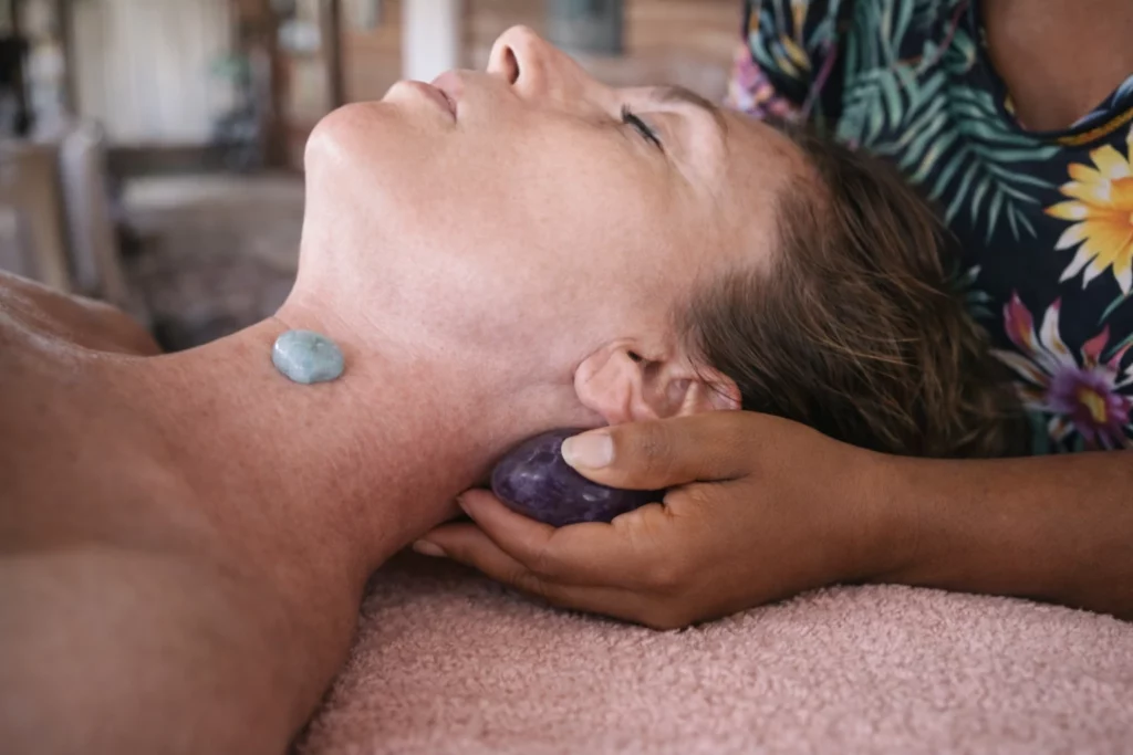 Massage aux pierres semi-précieuses avec aigue-marine au centre de la gorge dans une ambiance douce et apaisante